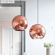Two rose gold copper sphere pendant lights with polished surfaces hang from black cords for kitchen bar use