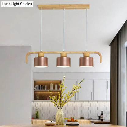 Modern rose gold drum island chandelier with three copper cylindrical shades and light wood frame for dining table lighting