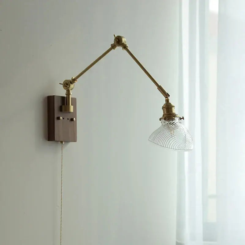 Adjustable modern rotatable brass wall light fixture with clear ribbed glass shade and dark wood mounting plate for stairs