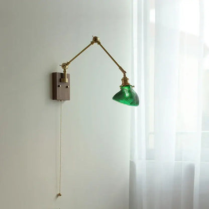 Modern rotatable brass wall light fixture with green ribbed glass shade mounted on articulated arm with wooden base and pull chain