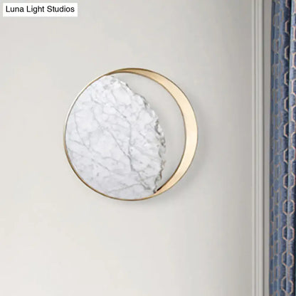 A modern round gold and white marble led wall sconce with a gold-toned metallic frame for bedroom use