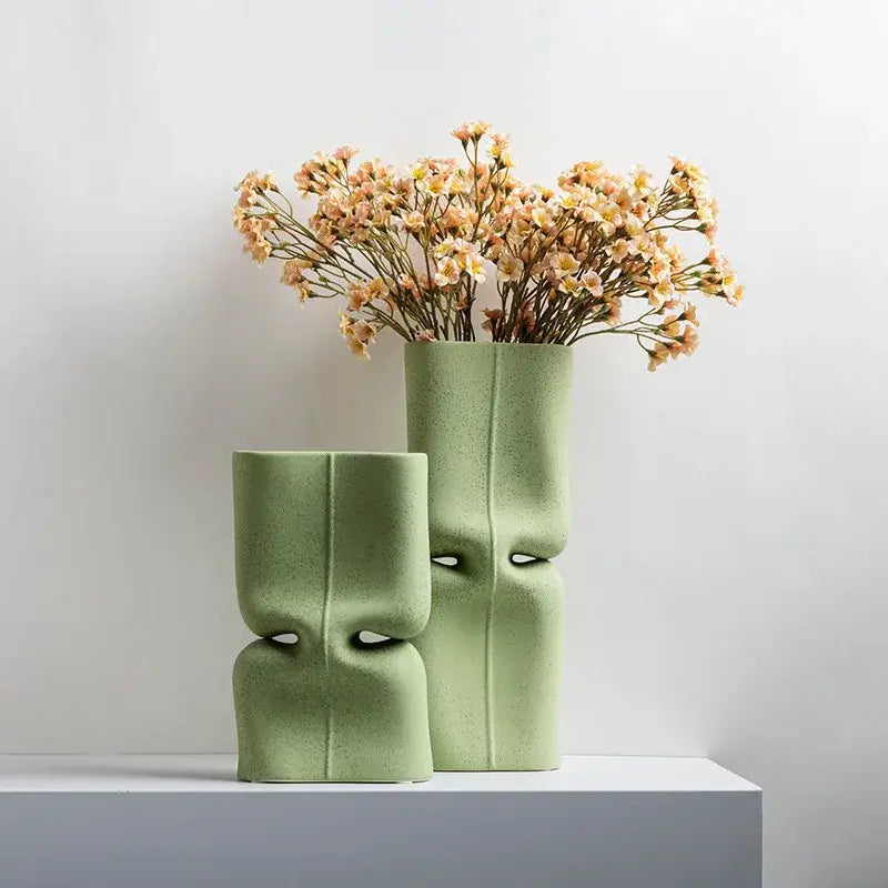Two matte sage green hollow ceramic vases with sculpted face designs for modern living room decor