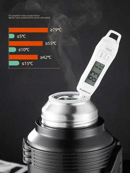 White digital thermometer inserted into the opening of a modern silver and black insulated kettle with glass liner and folding handle