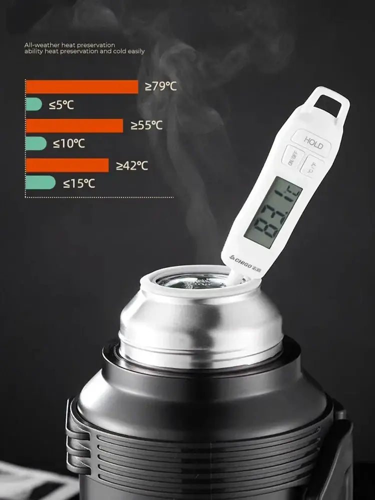 White digital thermometer inserted into the opening of a modern silver and black insulated kettle with glass liner and folding handle