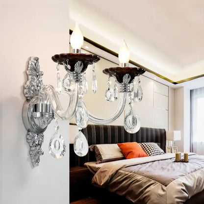 Modern silver candle wall mounted sconce with chrome ornate arms, dark brown ceramic bases, and clear glass teardrop crystals
