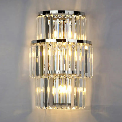Modern silver crystal three-tiered wall mounted light with cascading clear prisms and polished chrome rings emitting warm glow