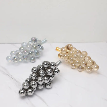 Three metallic crystal grape decorative sculptures in silver gold and chrome finishes on a marble surface