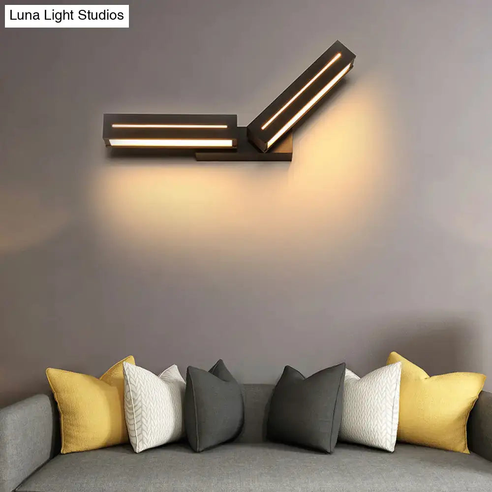 Modern black wall mounted light with two angled illuminated rectangular panels casting a warm glow for bedroom use
