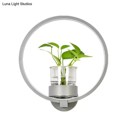 Modern silver wall light with sleek metallic frame and clear glass plant pot housing green leaves 110v-120v bedroom sconce