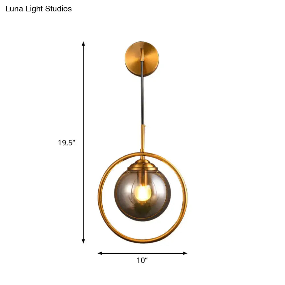 Gold-toned modern bedroom wall sconce with a circular frame and smoke gray clear glass globe compatible with 220v-240v and 110v-120v