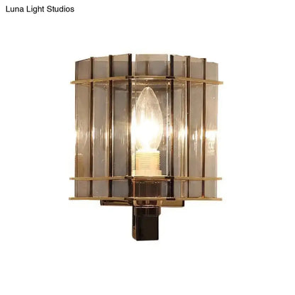 Brass-framed modern wall light with vertical smoke gray glass panels and central incandescent bulb for bedroom use