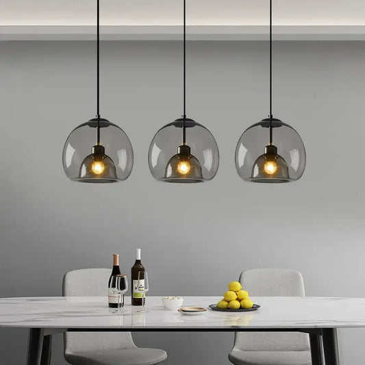 Three modern smoke gray glass pendant lights with black cords hang above a dining table chandelier