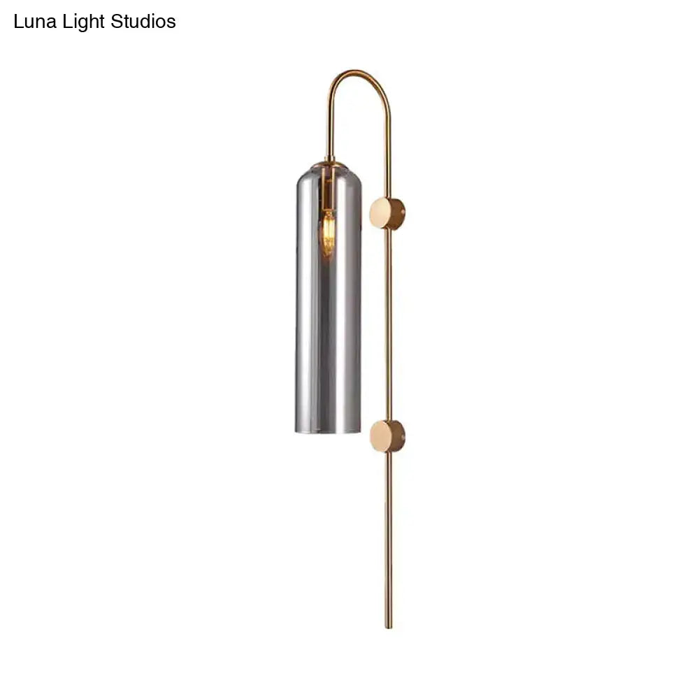A sleek modern living room wall light with smoke gray cylindrical glass shade and brass arms accented by wooden discs
