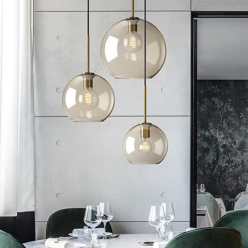 Three spherical modern smoked glass pendant lights with brass accents hanging from the ceiling for dining room use
