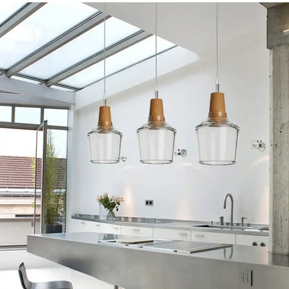 Three modern pendant lights with clear glass shades and warm wood tops for dining room lighting