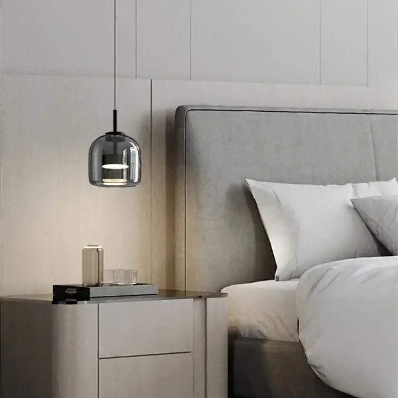 A modern smoked gray glass led pendant chandelier with black metal fixture hanging above a bedside table