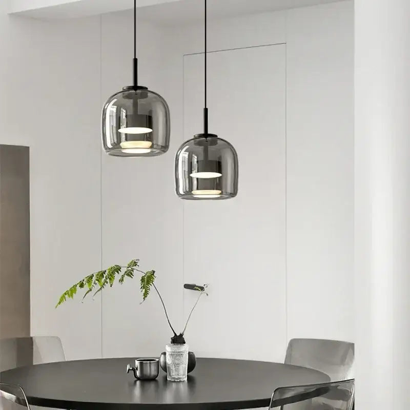 Two sleek modern smoked gray glass led pendant chandelier lights with black metal fixtures hang above a dining table