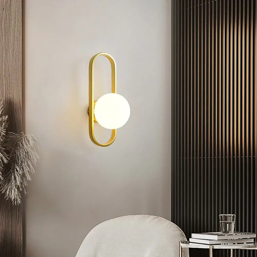 Modern spherical glass shade gold wall lamp with a gold-toned minimalist frame and frosted glass globe bulb for bedroom