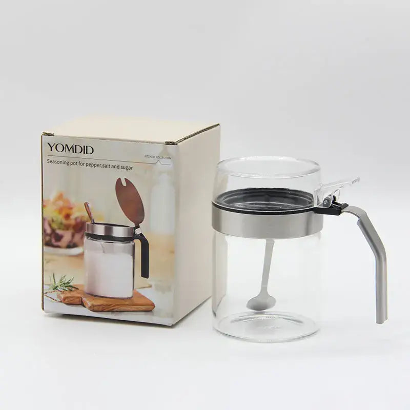 Clear glass seasoning pot with silver metal lid and handle featuring an integrated spoon for kitchen supplies
