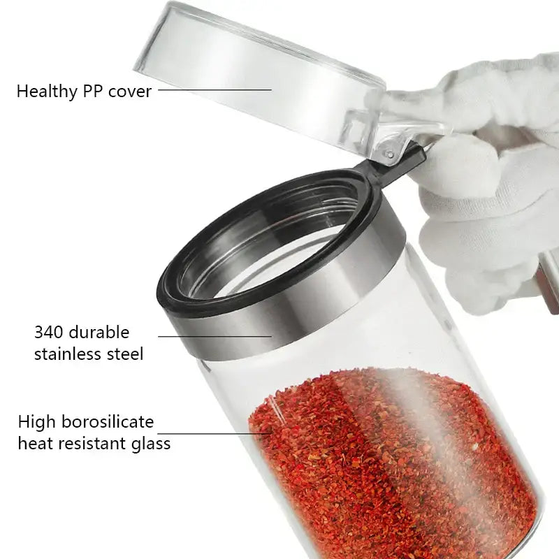Modern stainless steel and glass seasoning pot with clear plastic lid filled with vibrant red chili flakes