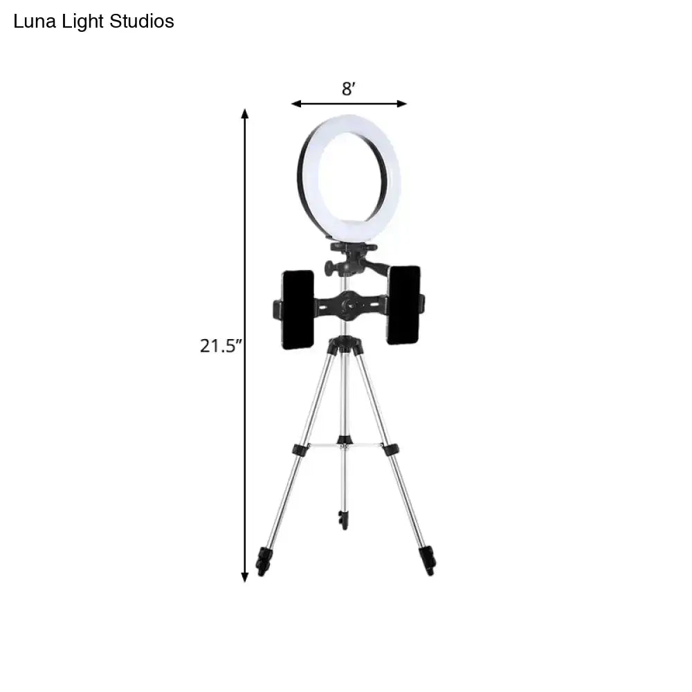 A modern style black and silver led flash light ring with white illumination mounted on a tripod with phone holders