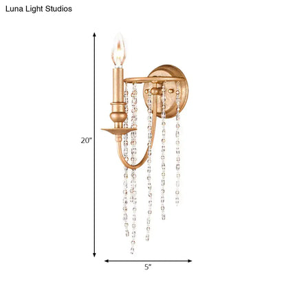 Modern style gold sconce with clear crystal beaded strand and single candle-style bulb for bedroom lighting