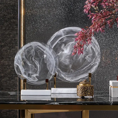 Two translucent swirling glass orbs with gold stands on white marble bases home decor figurines geometric disk design