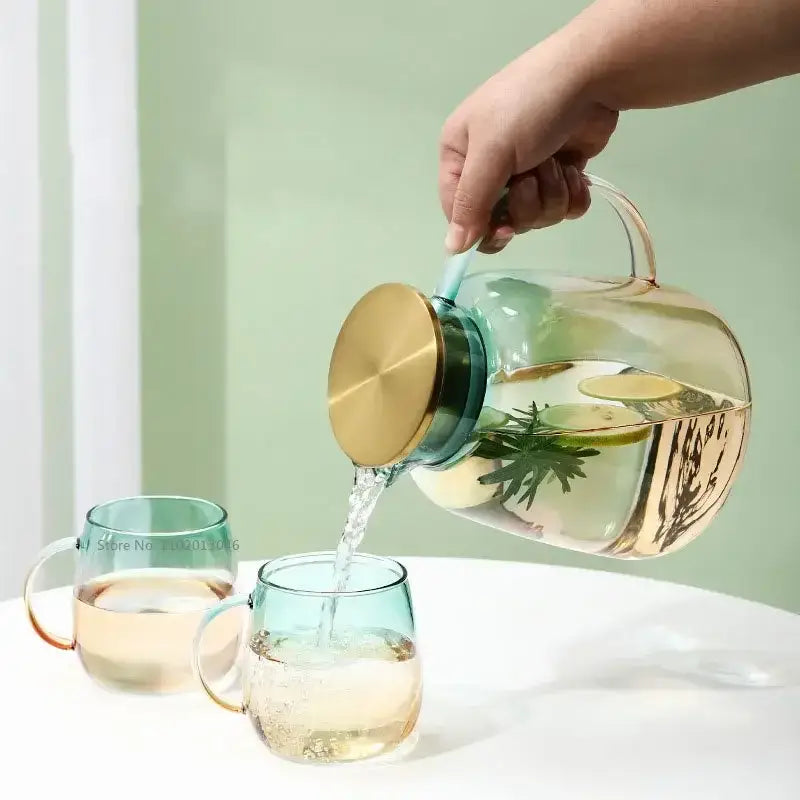 Clear glass teapot with gold-toned lid and handle filled with infused water in modern teal and gold glass teapot set