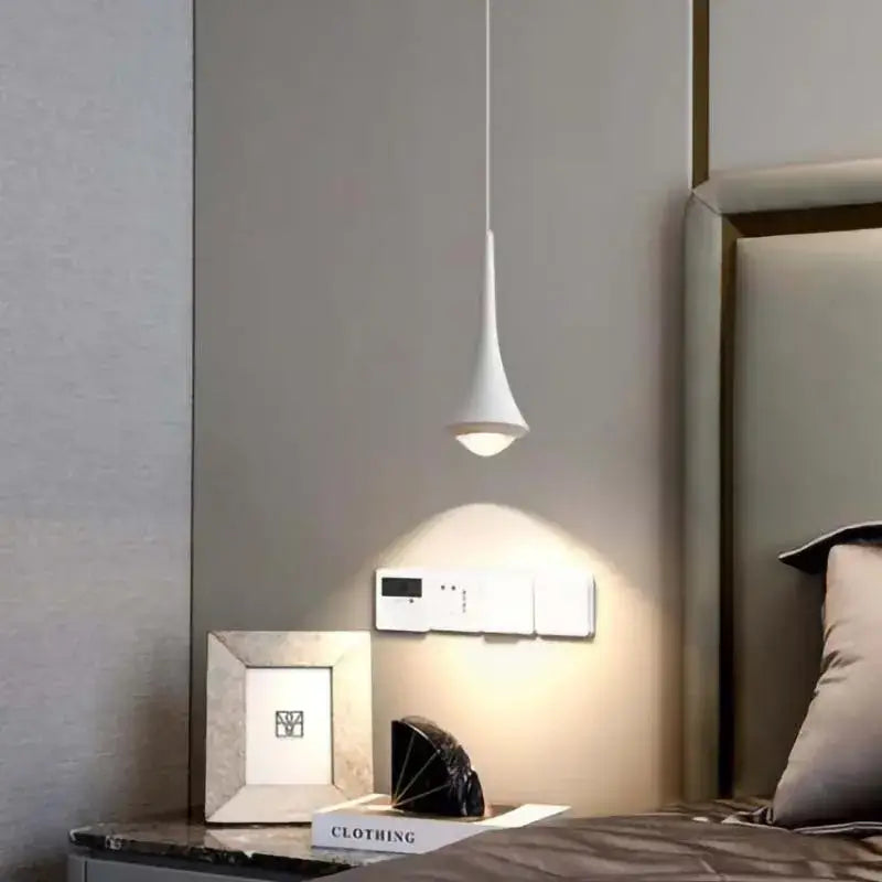 A sleek white teardrop pendant light with a gold black and white cord pendant light design above a bedside table