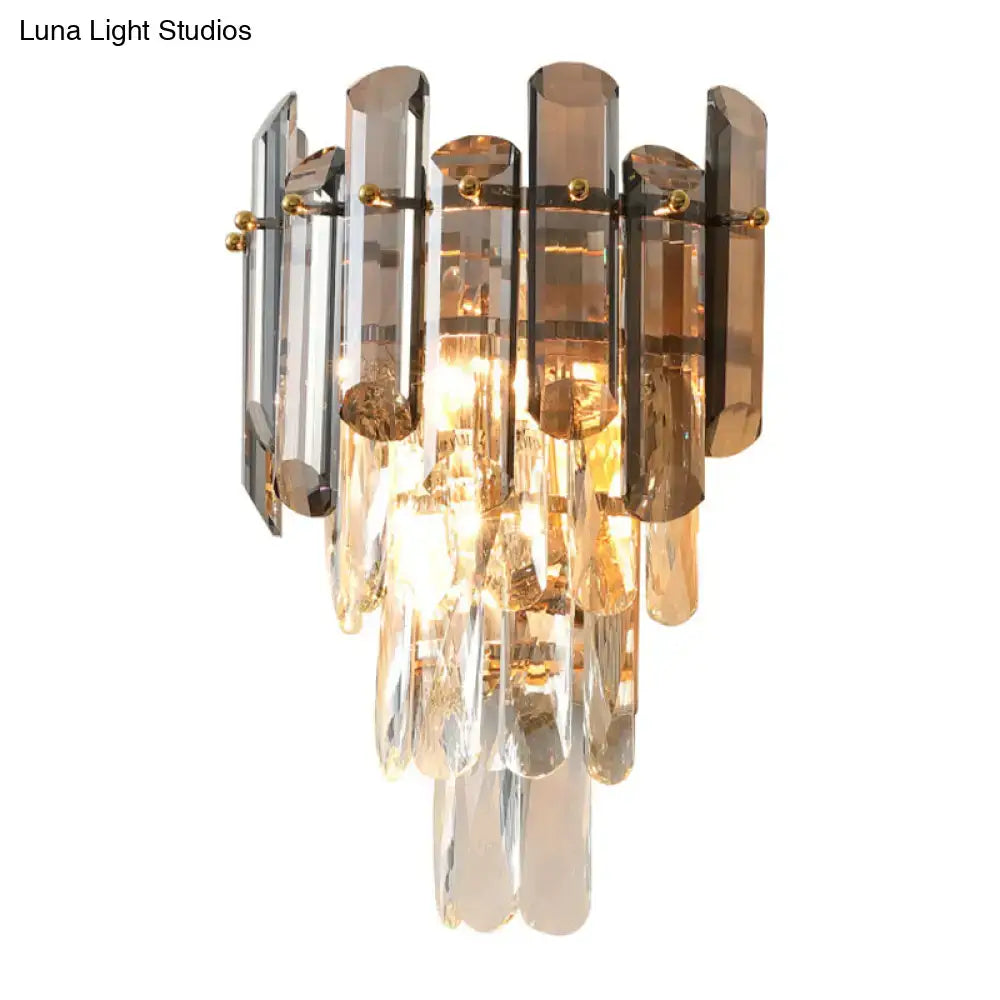 Elegant modern tiered clear wall sconce with cascading amber and clear crystal prisms and gold metal accents for bedroom lighting