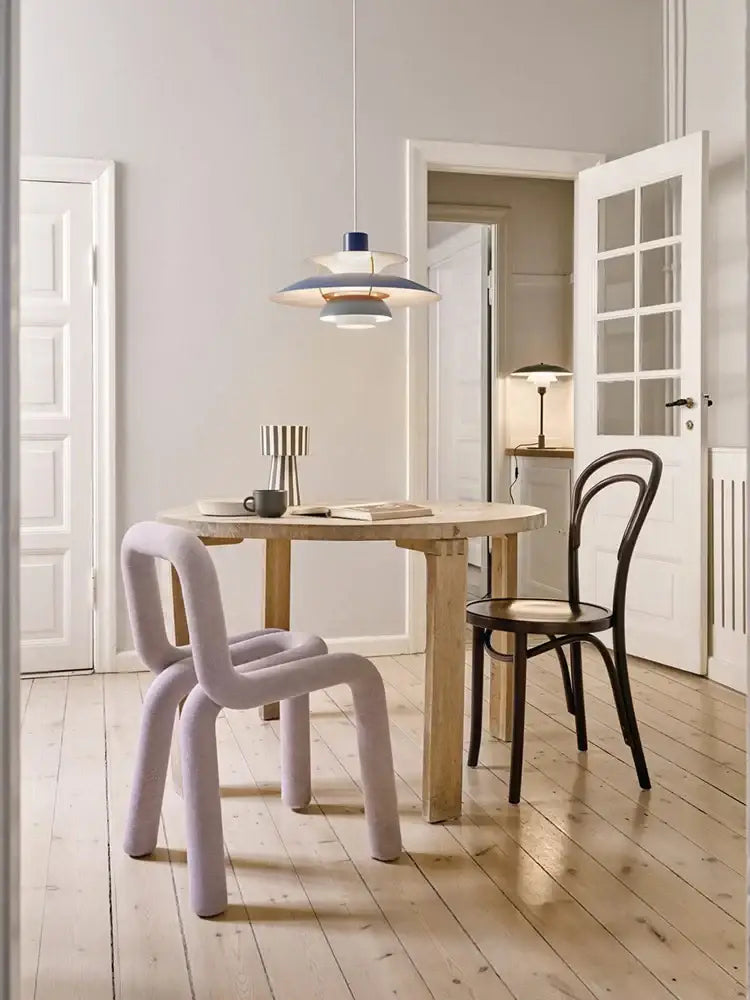 Pastel lavender upholstered chair with sculpted tubular frame paired with modern tiered colorful metal hanging light suspension lamp by decorbites danish designer