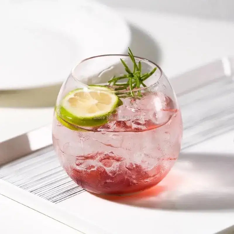 Modern transparent glass coffee mug filled with pink iced drink garnished with lime slice and rosemary sprig