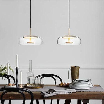 Two modern tricolor glass pendant lights with brass accents hang above a dining room table