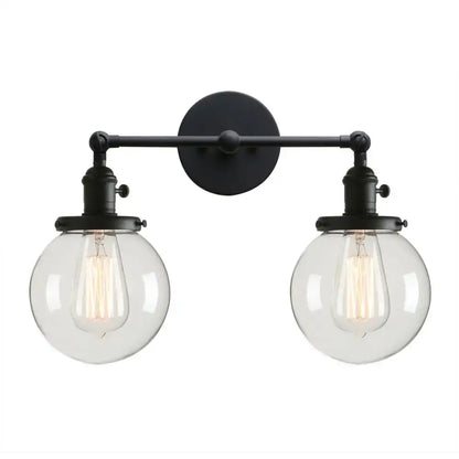 Black wrought iron wall sconce with double ball heads clear glass globes and exposed filament bulbs for bedroom use