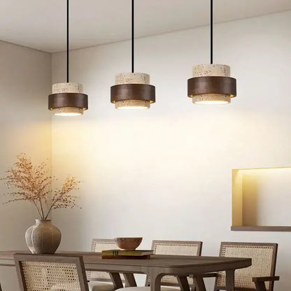 Three modern beige and dark bronze stone pendant lights with speckled cylindrical shades hang above a dining table