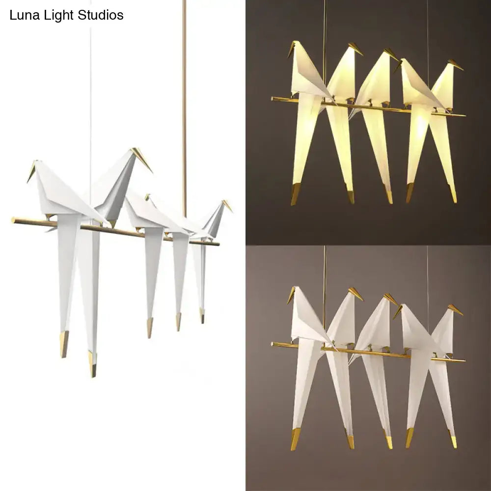 White origami bird shaped pendant light with gold tipped feet and beaks hanging on a slender brass island pendant light rod
