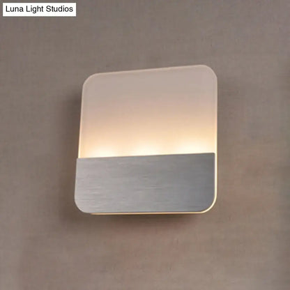 Modern white and silver led sconce light with frosted glass top and brushed metal base emitting warm glow for bedroom