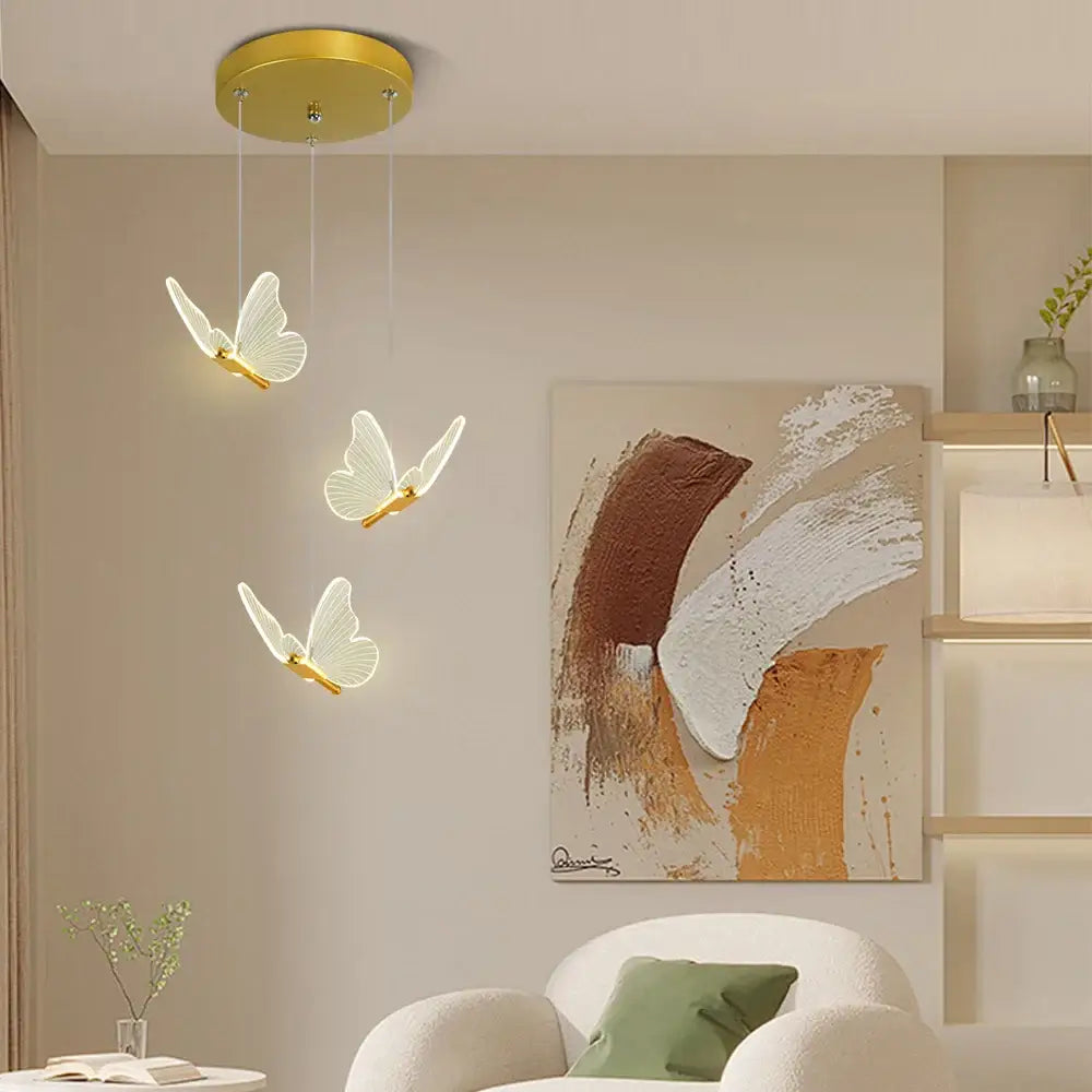 Three white butterfly pendant lights with warm gold finish hang from a circular warm gold ceiling fixture