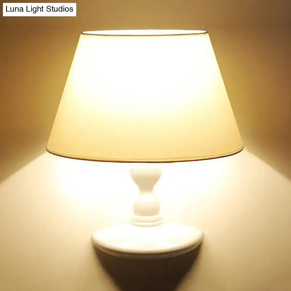 A warm white black cone ceramic wall sconce with a fabric shade and turned wood base for bedroom lighting