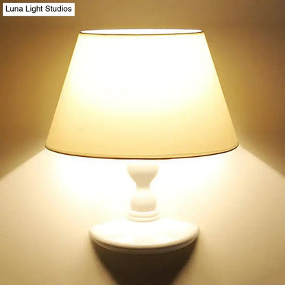 A warm white black cone ceramic wall sconce with a fabric shade and turned wood base for bedroom lighting