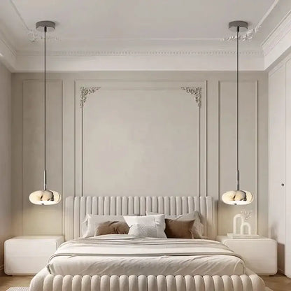 Cream-colored tufted bed with plush headboard and footboard featuring a modern white marble bedside pendant light