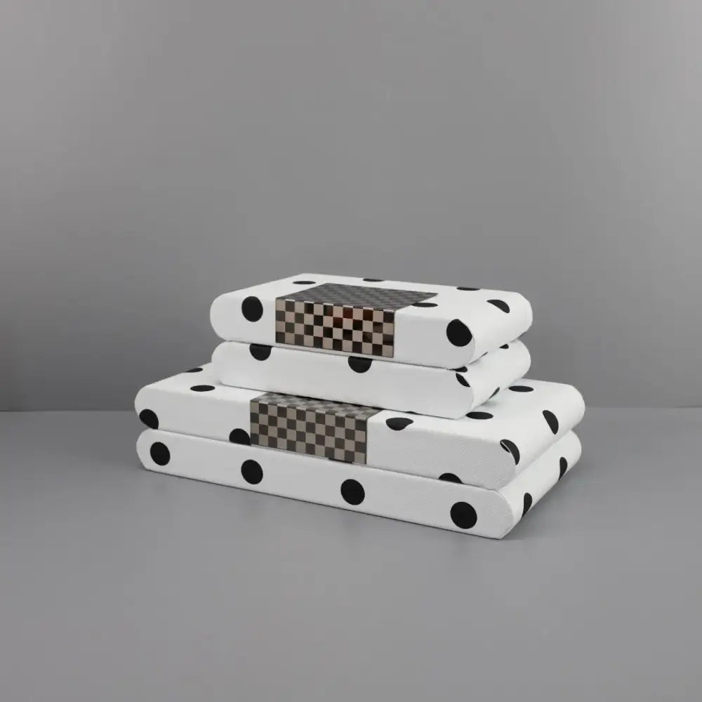 Stacked white polka dot leather storage box notebooks with black dots and brown-gray checkered accent panel on spine