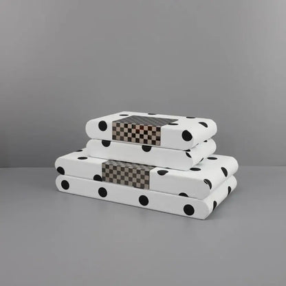 Stacked white polka dot leather storage box notebooks with black dots and brown-gray checkered accent panel on spine