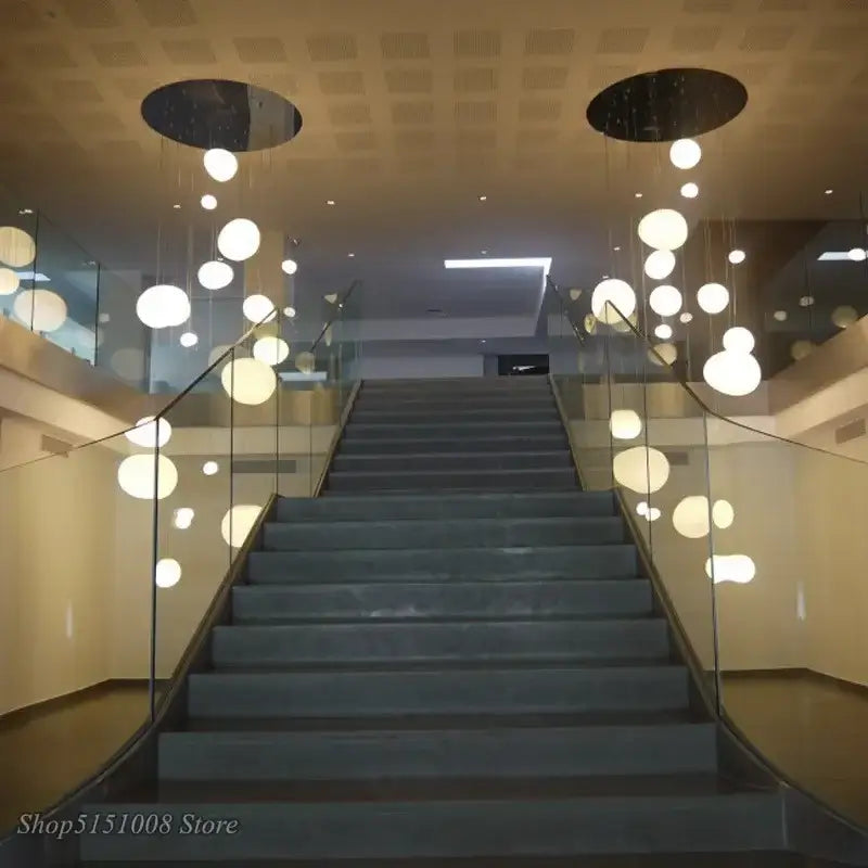 Modern white cascading glass pendant light with suspended spherical glass pendant lights on a gray stone staircase