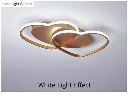 Gold-toned modern white coffee pendant light with two interlocking heart-shaped rings outlined in white led lighting