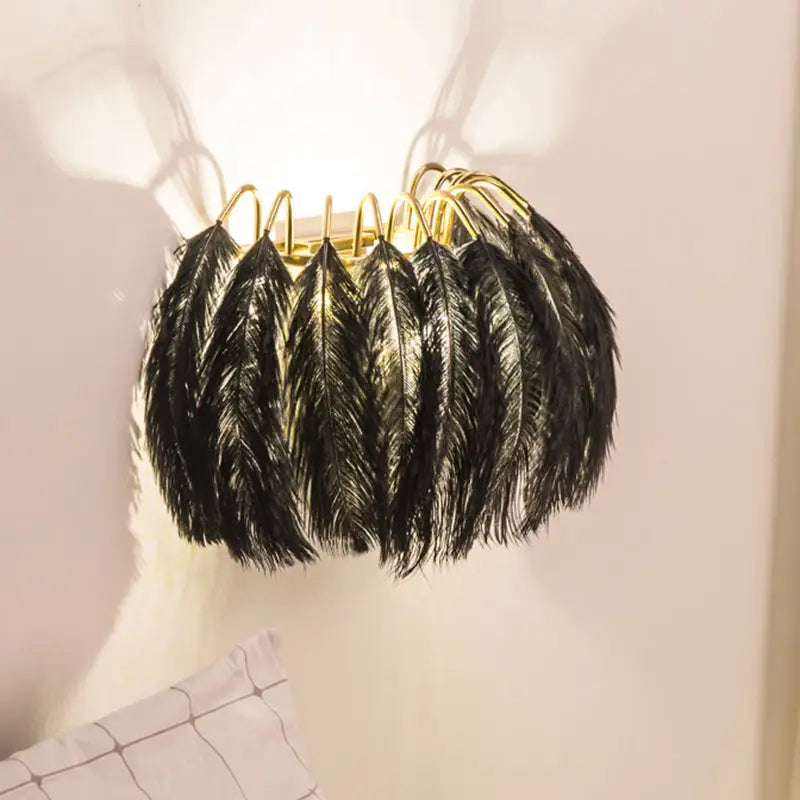Modern metal wall sconce featuring black ostrich feathers and a gold-toned metal frame for bedroom lighting
