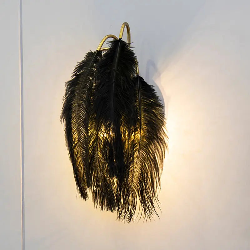 Modern metal wall sconce featuring black ostrich feathers with a gold-toned metal frame for bedroom lighting