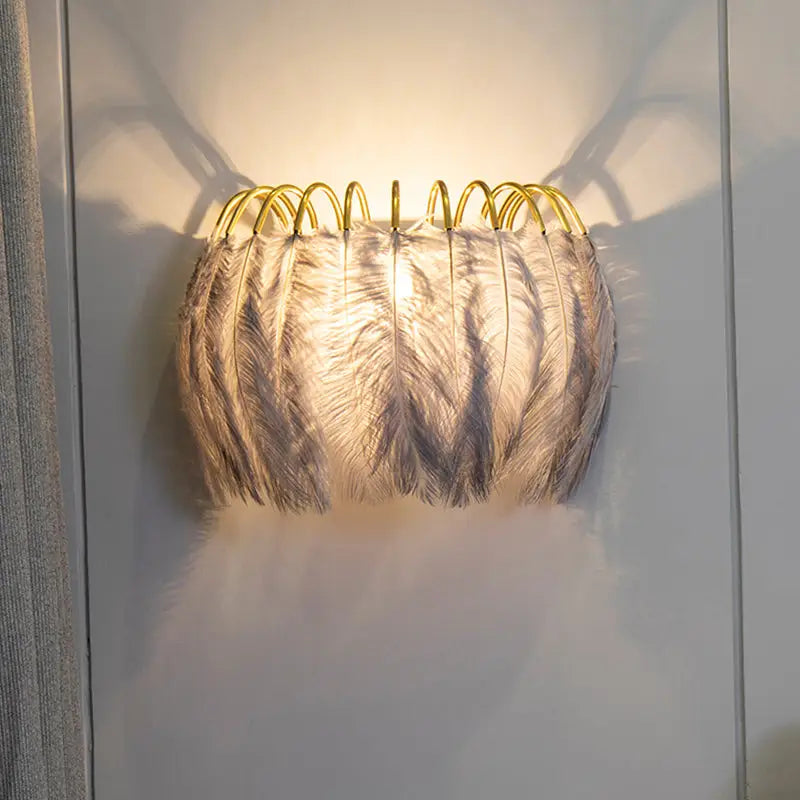 Modern metal wall sconce with a golden frame and white feather shade for bedroom lighting