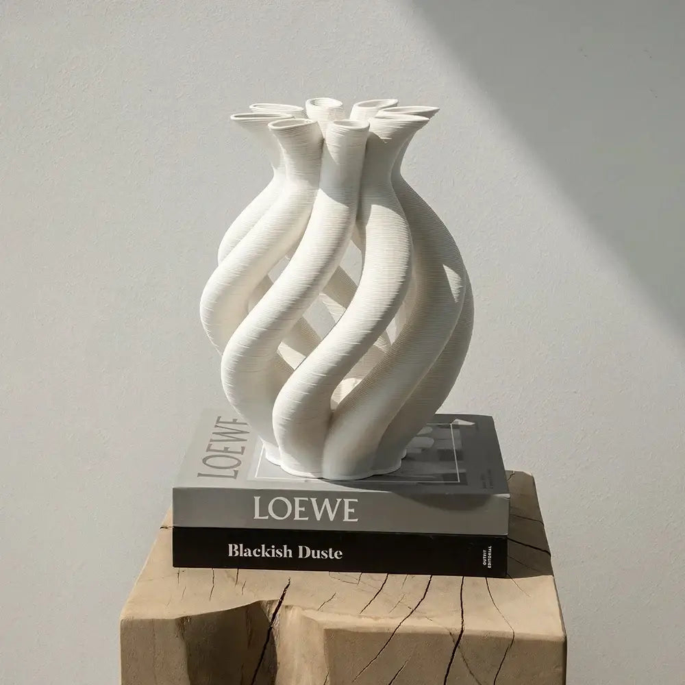 A sleek white geometric ceramic hollow vase with a twisted design on stacked loewe books for living room decor