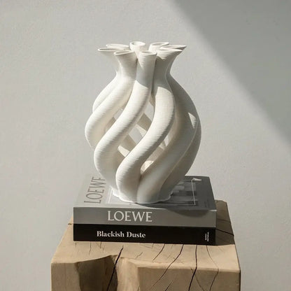 A sleek white geometric ceramic hollow vase with a twisted design on stacked loewe books for living room decor